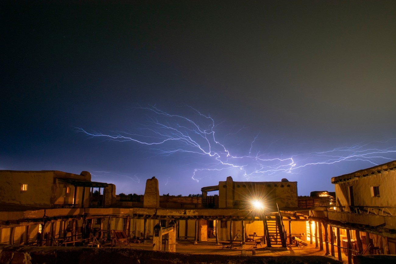 A storm over Bent's Old Fort A night sky with streaks of lightning is above the adobe fort.
