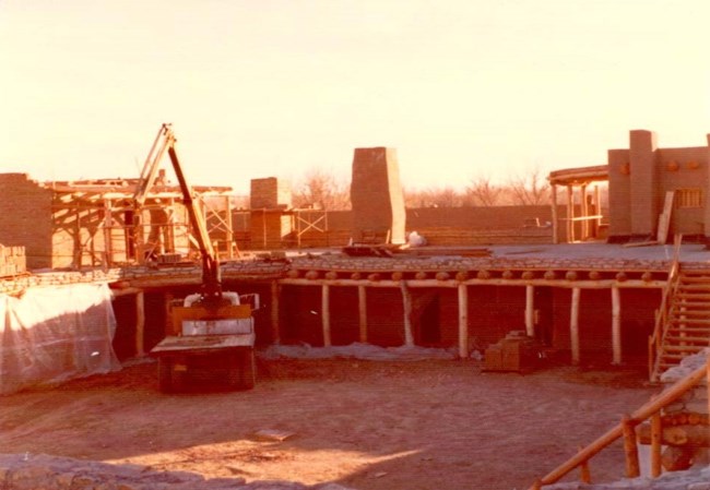 A crane truck is positioned next to the edge of a plaza. The building is in a state of construciton, and clearly not finished.