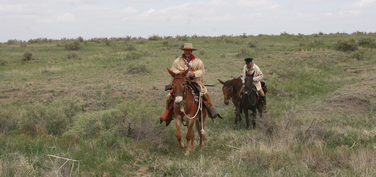 Two riders on horseback travel on a prairie landscape