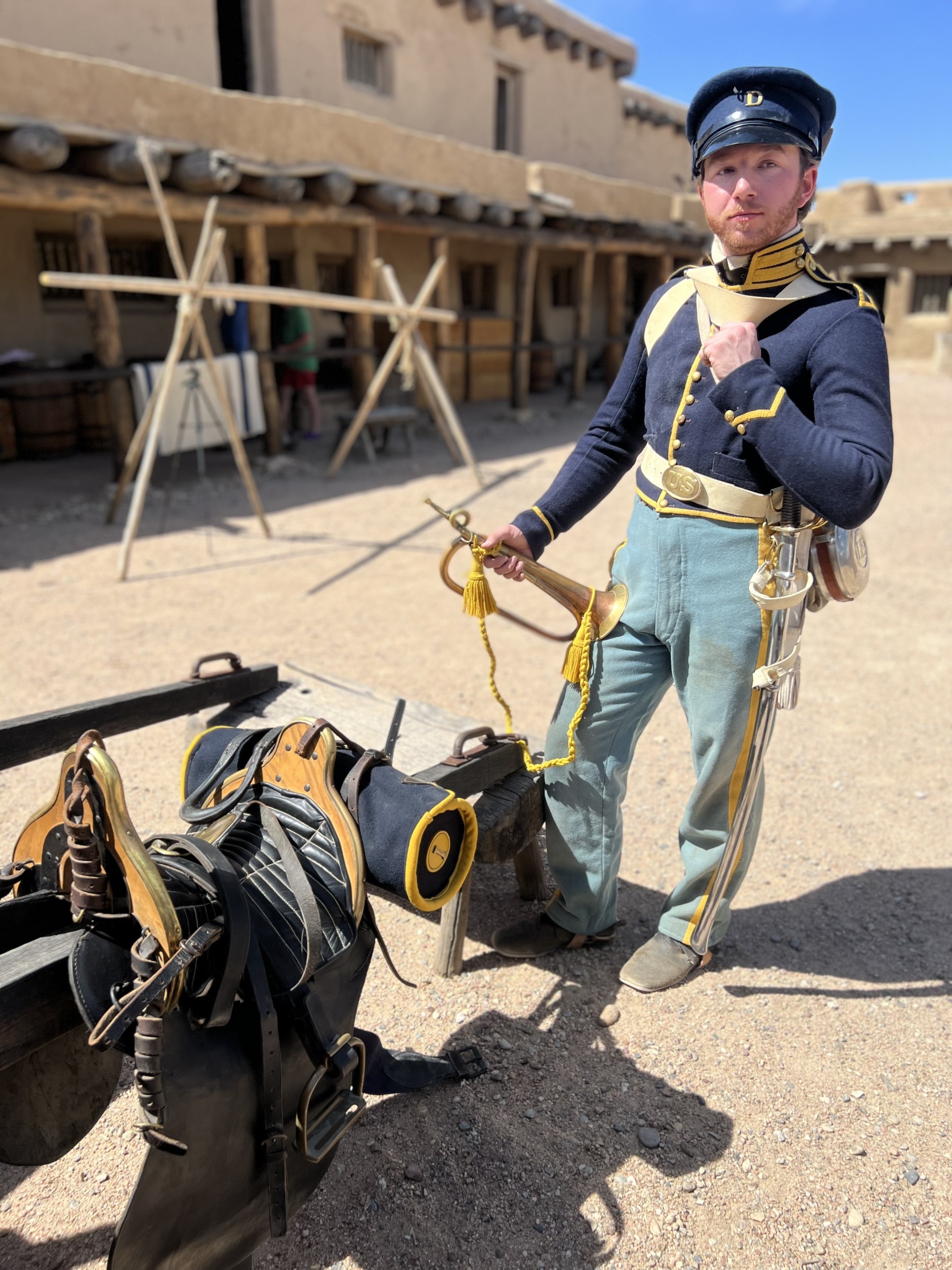 Dragoon in Fort A man dressed in a historic military uniform stands next to saddles on display.