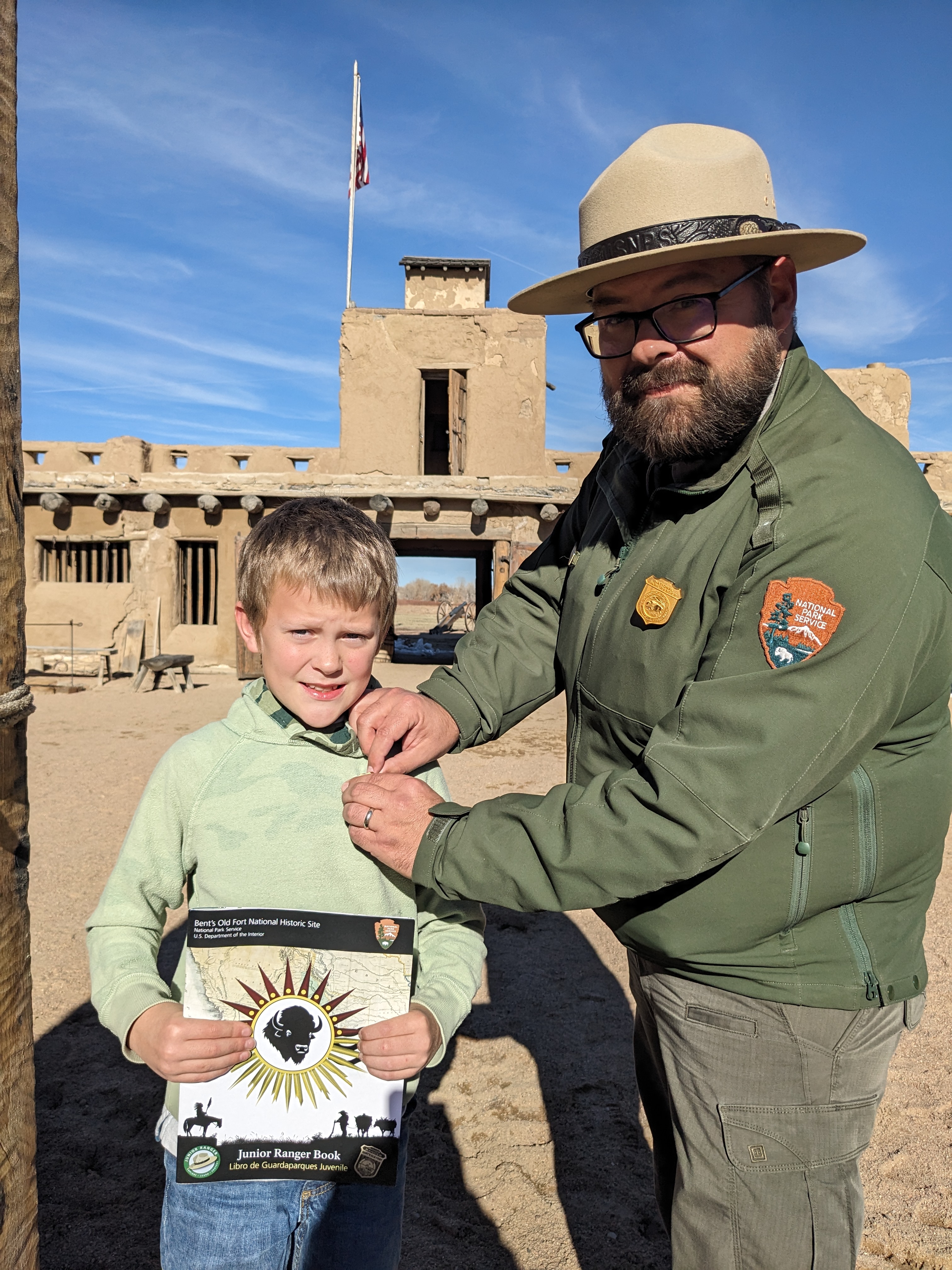 A park ranger pins a junior ranger badge on a young visitor.