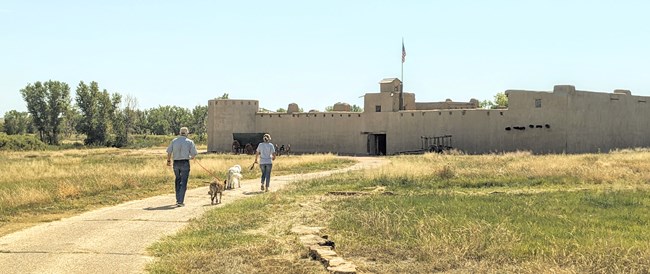 Couple walks path to fort with two dogs on leash