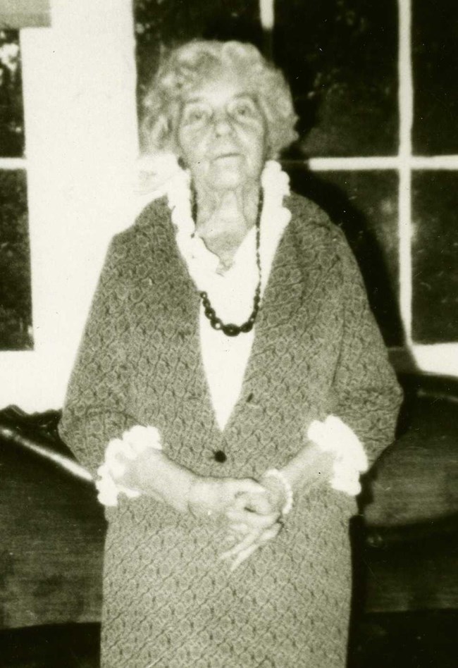 Alice Paul standing in Belmont House indoor terrace with hands clasped in front