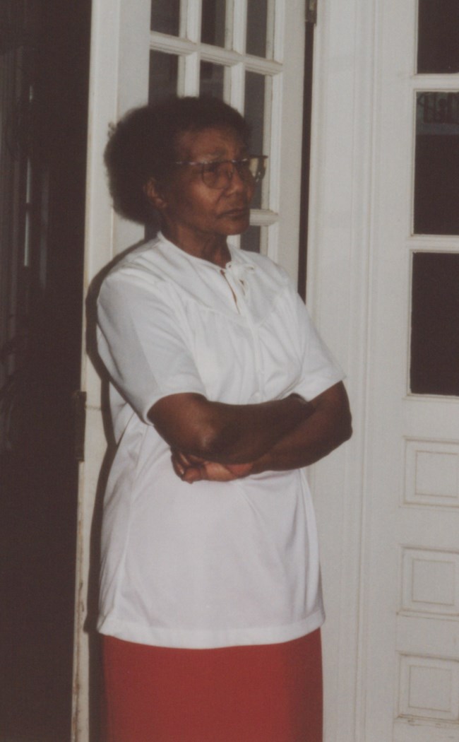 Letha Mae Glover standing in indoor terrace of Belmont House with arms crossed