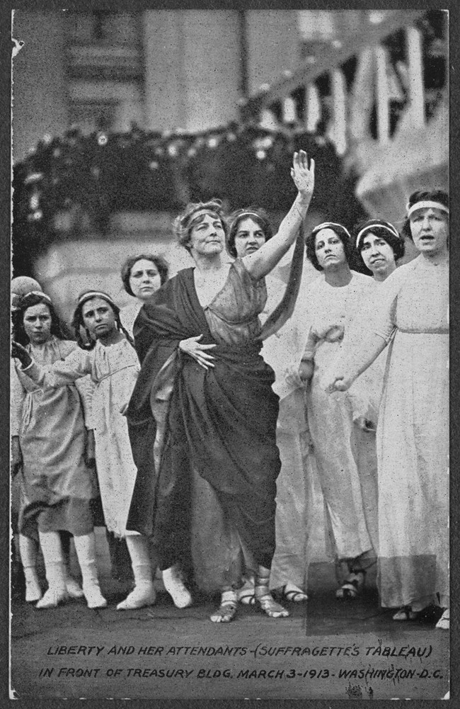 Photograph of women and girls in Greek costume in suffrage tableau in front of the Treasury Building, Washington, D.C. Central figure is dressed in toga as Liberty.