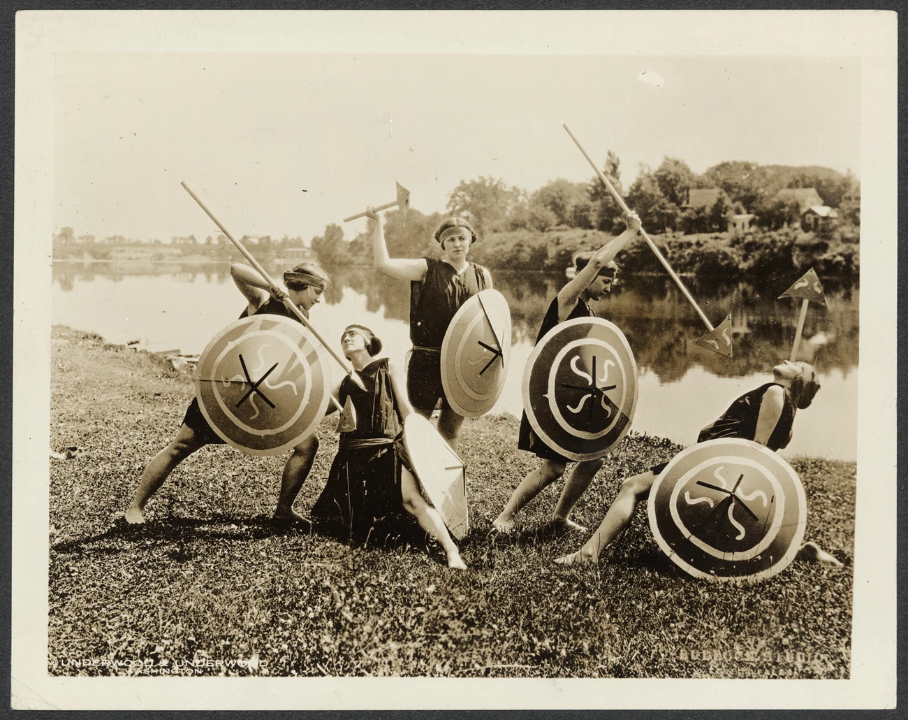 Seneca Falls pageant Photograph of five young women, in costume and holding shields and spears, posing in front of a lake.
