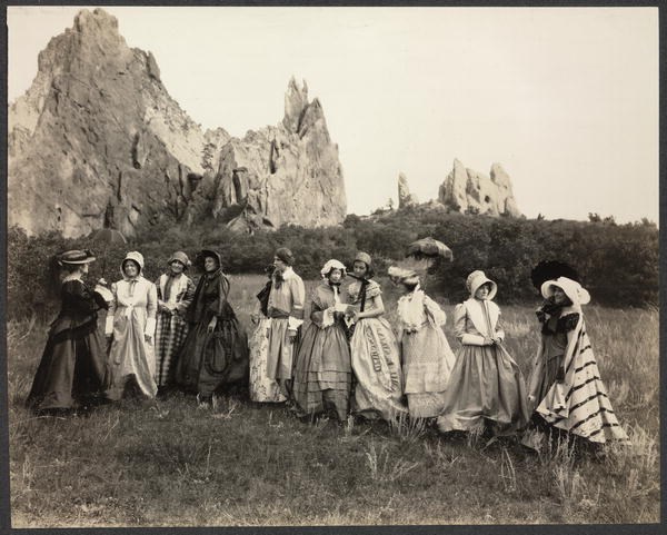 Women Pioneers Garden of Gods Photograph of group of women in nineteenth-century costume standing outside, large rock formation in background.