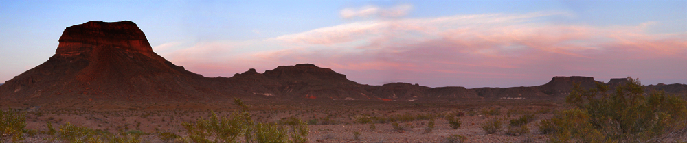 A line of hills and a mountain are highlighted red and pink by the setting sun.