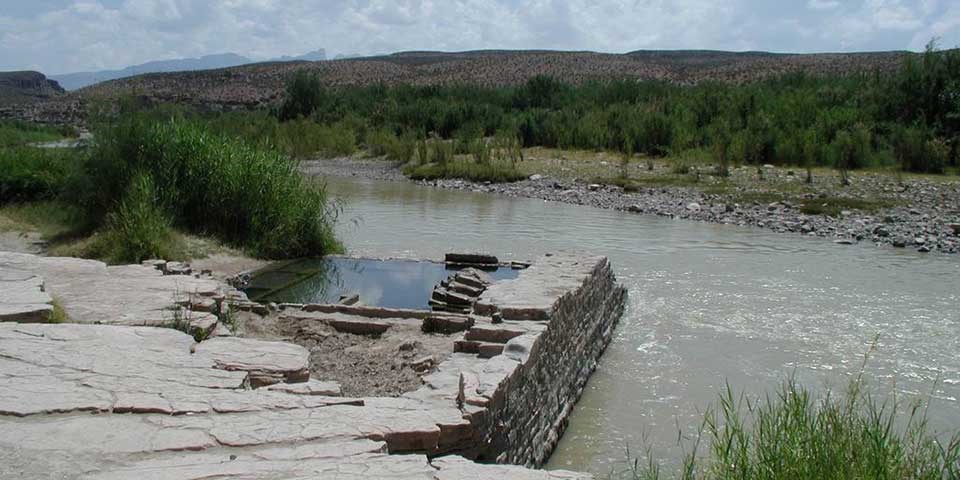 The stone foundation of a hot springs bath house remains abuts a river.