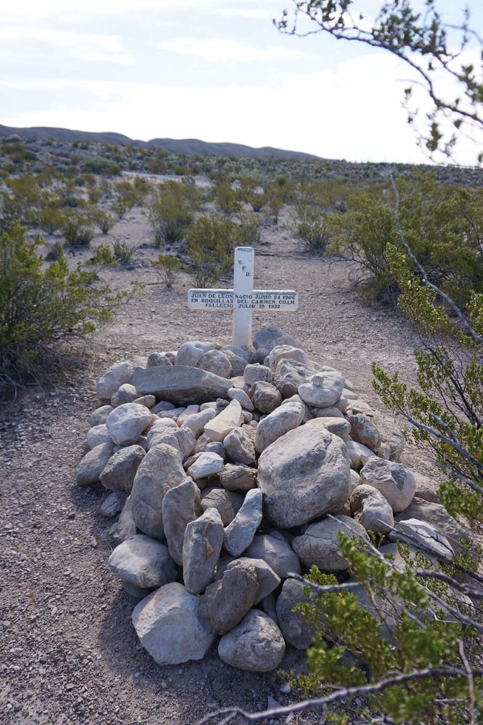 A cross headstone marks a grave with rocks piled on it.