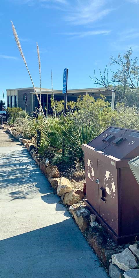 Metal recycling bins stand by the sidewalk to a national park visitor center building.