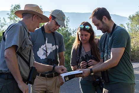 3 folks are standing with a ranger looking at a guide.