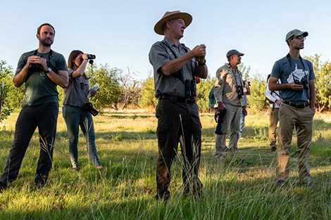 A male ranger leads a group of visitors on a bird walk.