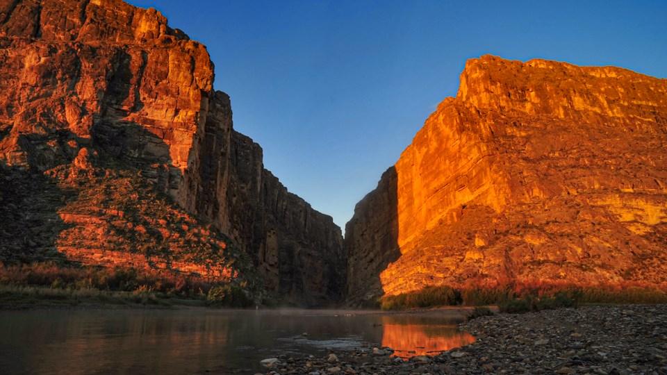 The light from a sunrise highlights two cliff faces in various colors.