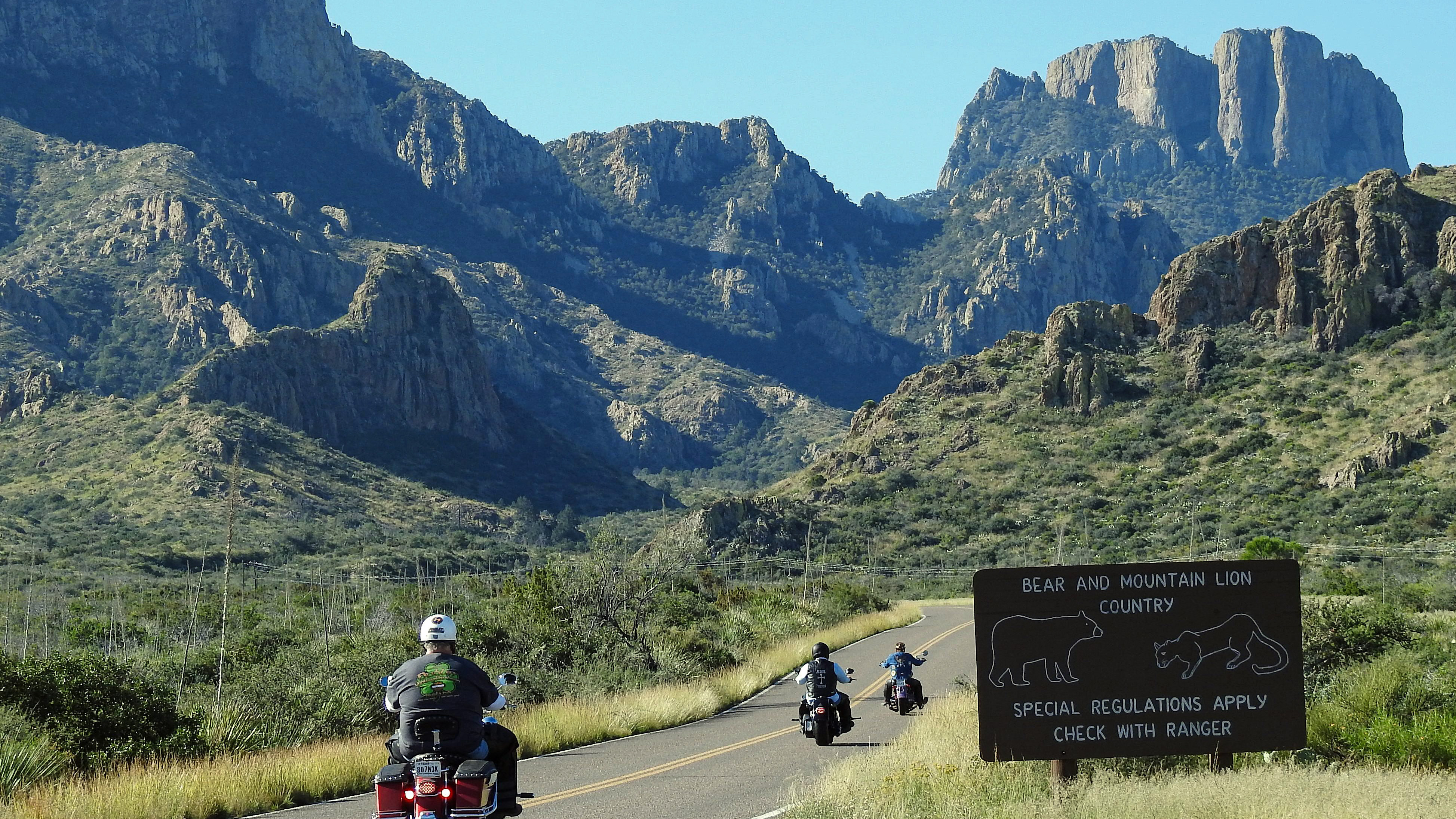 Three motorcycles are being ridden on a paved road into the mountains.