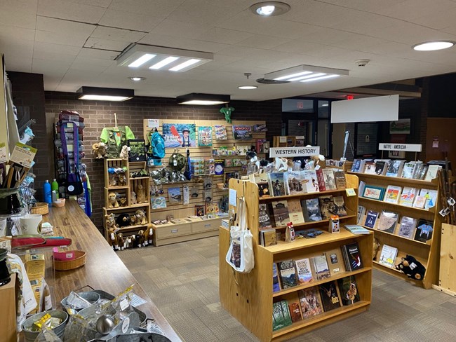 Several book shelves full of books surrounded by walls with games, toys, and tshirts.