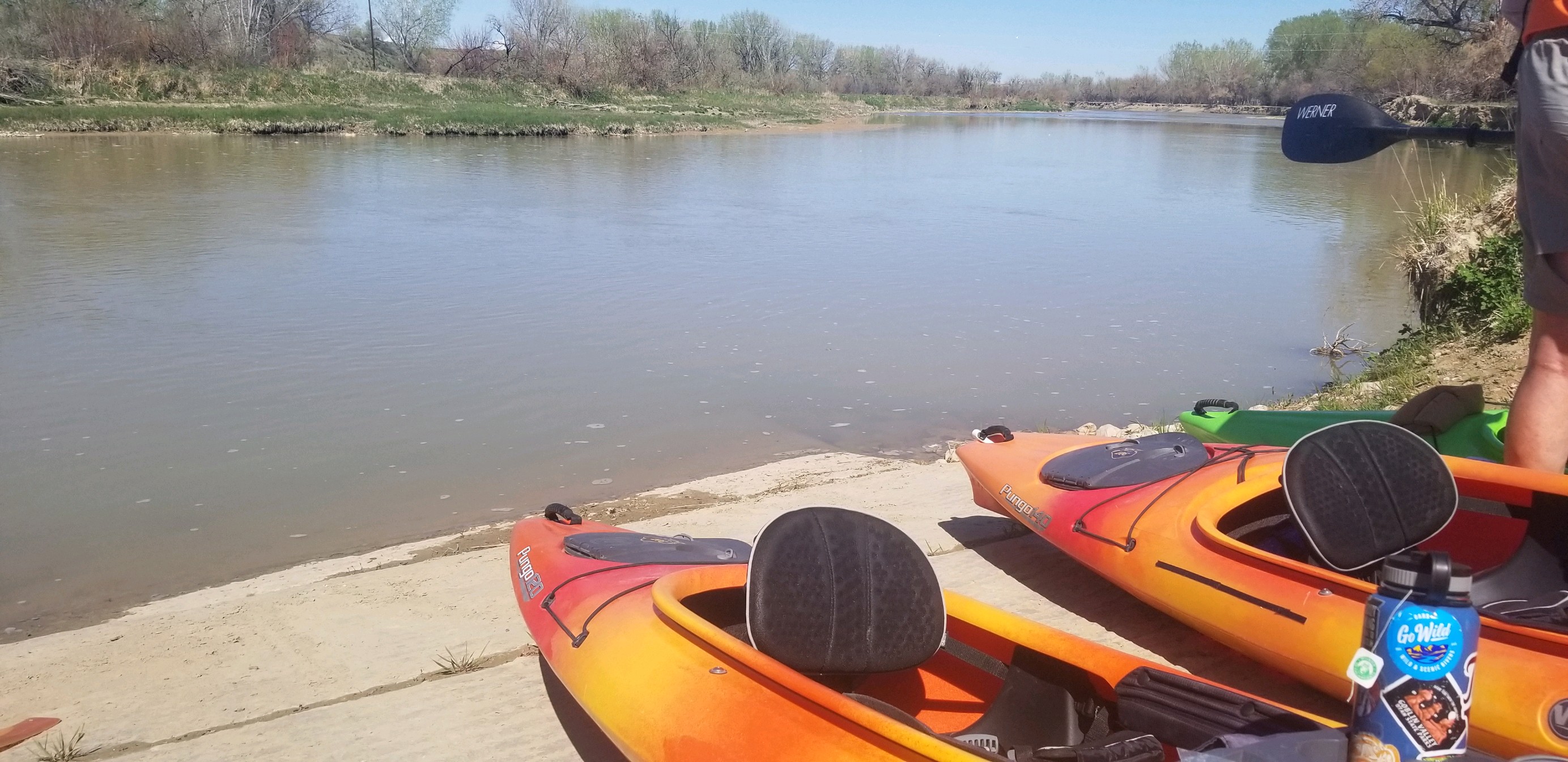 Two orange kayaks sit on a concrete boat ramp next to the river.