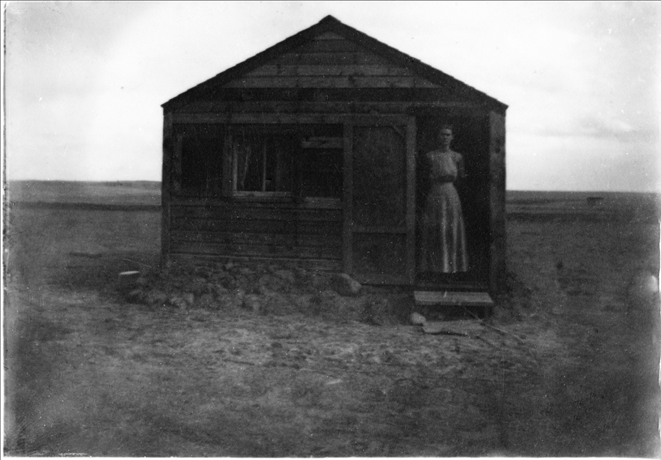 Amy McKinney's Grandma at her homestead Woman standing in the doorway of an early homestead.