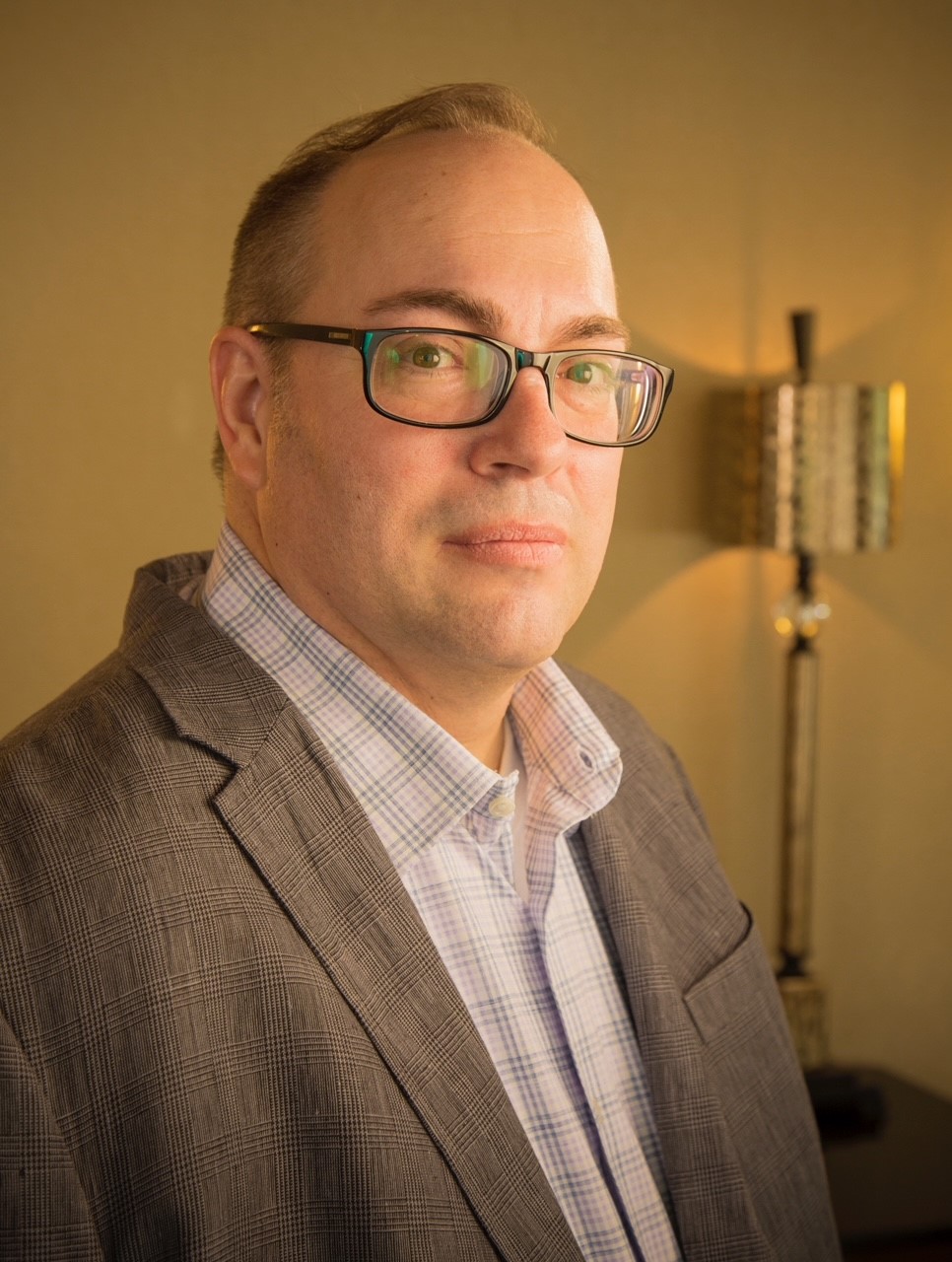 Len Mathieu, new AO for Powder River Group. Close up of Len Mathieu wearing glasses with a lamp in the background.