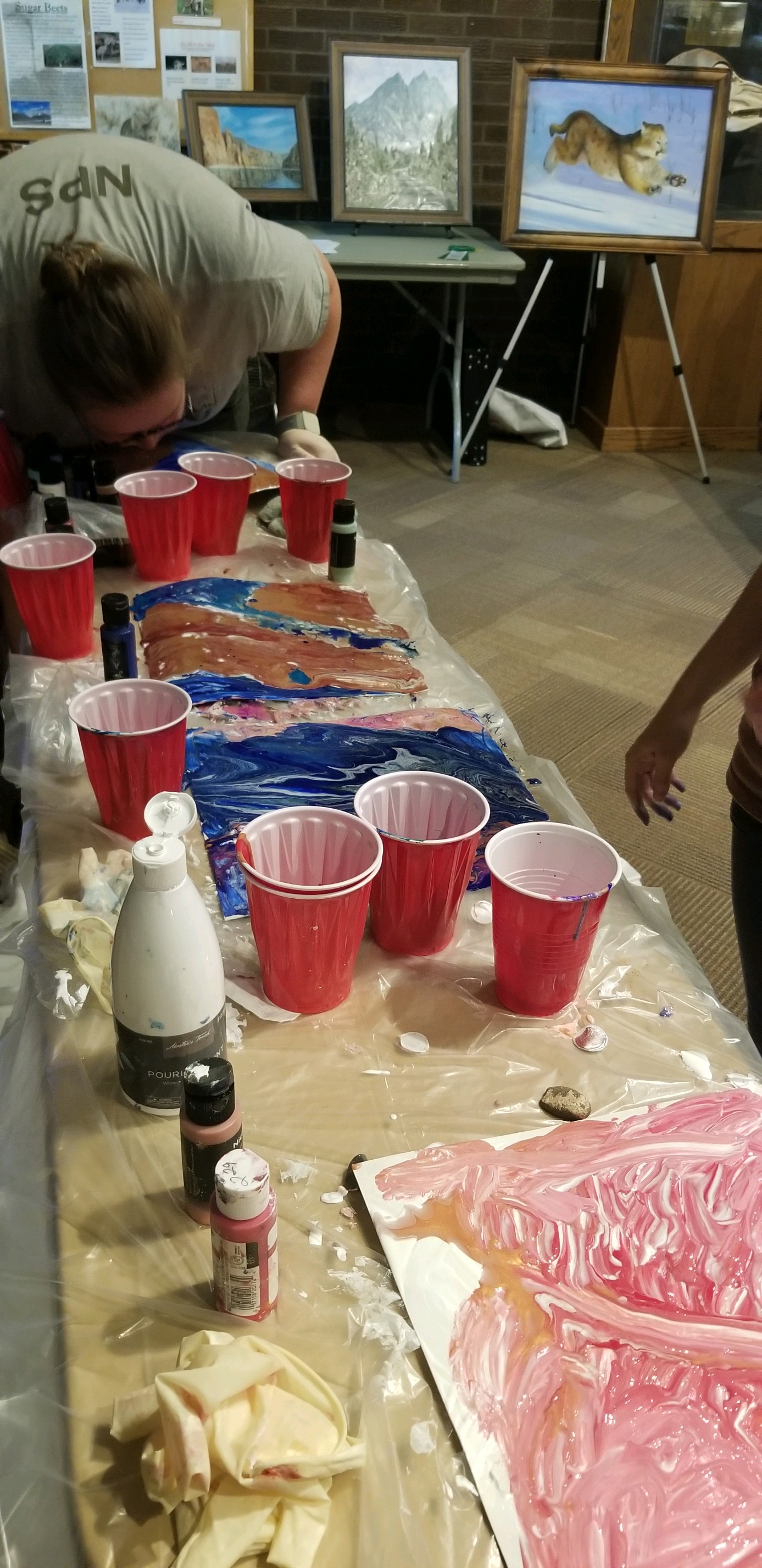 Pour Paint Program A table covered in plastic and red cups is used to pour paint on to paper to make art work using layers of paint.