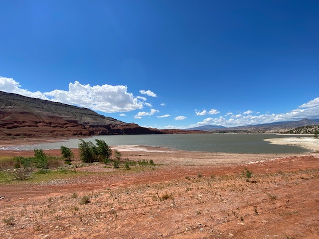 Large sand beach with water down low and red rocks in the background.