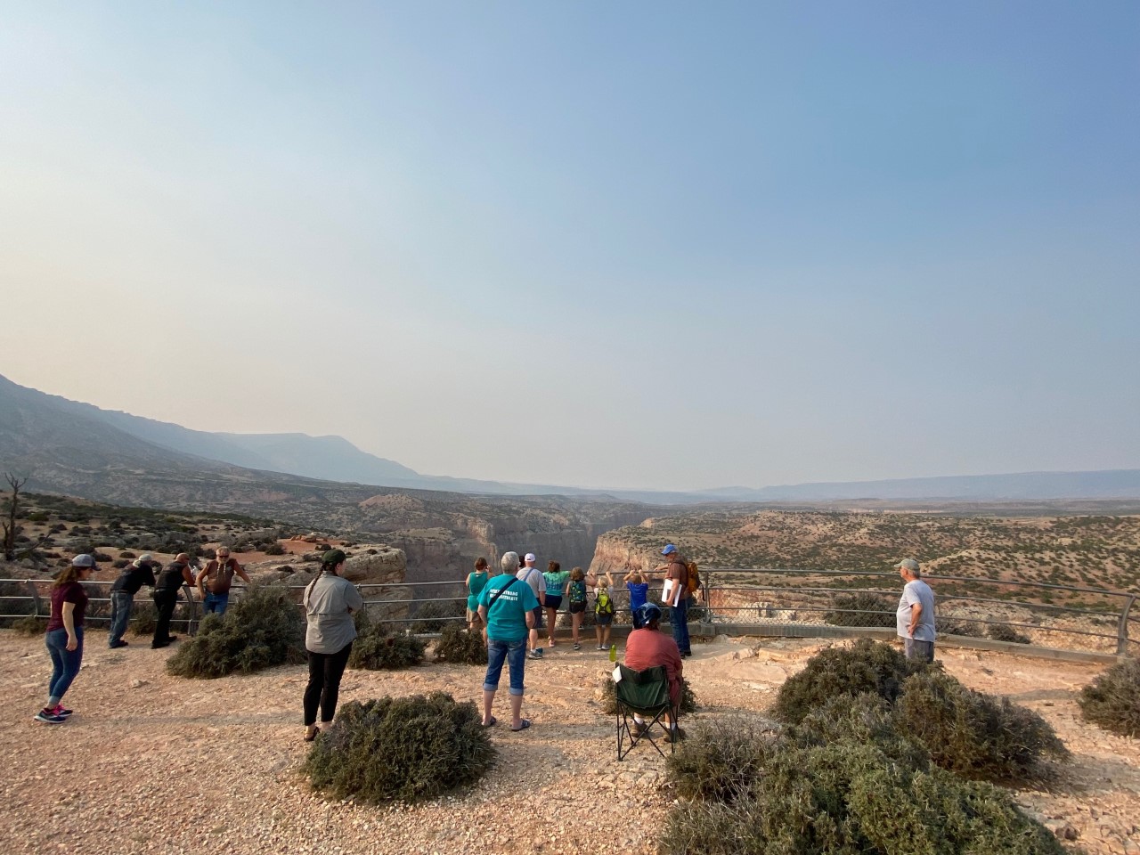 Several visitors are spread out listening to volunteer Greg discuss geology with the canyon overlook view in the background.