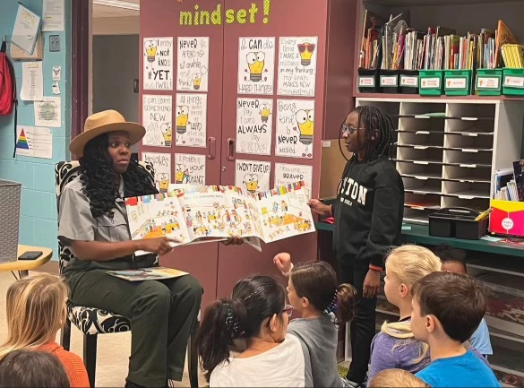 Ranger reading to students in a classroom. A ranger sits reading a book in front of a group of students.