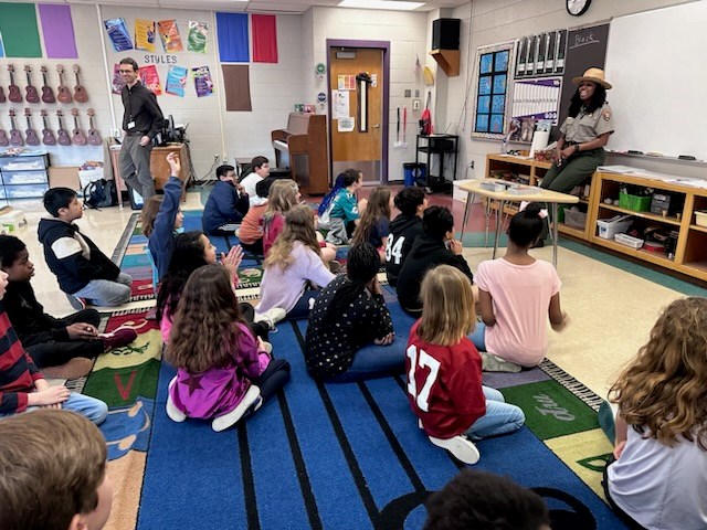 A ranger is talking in front of a group of about 20 seated students.