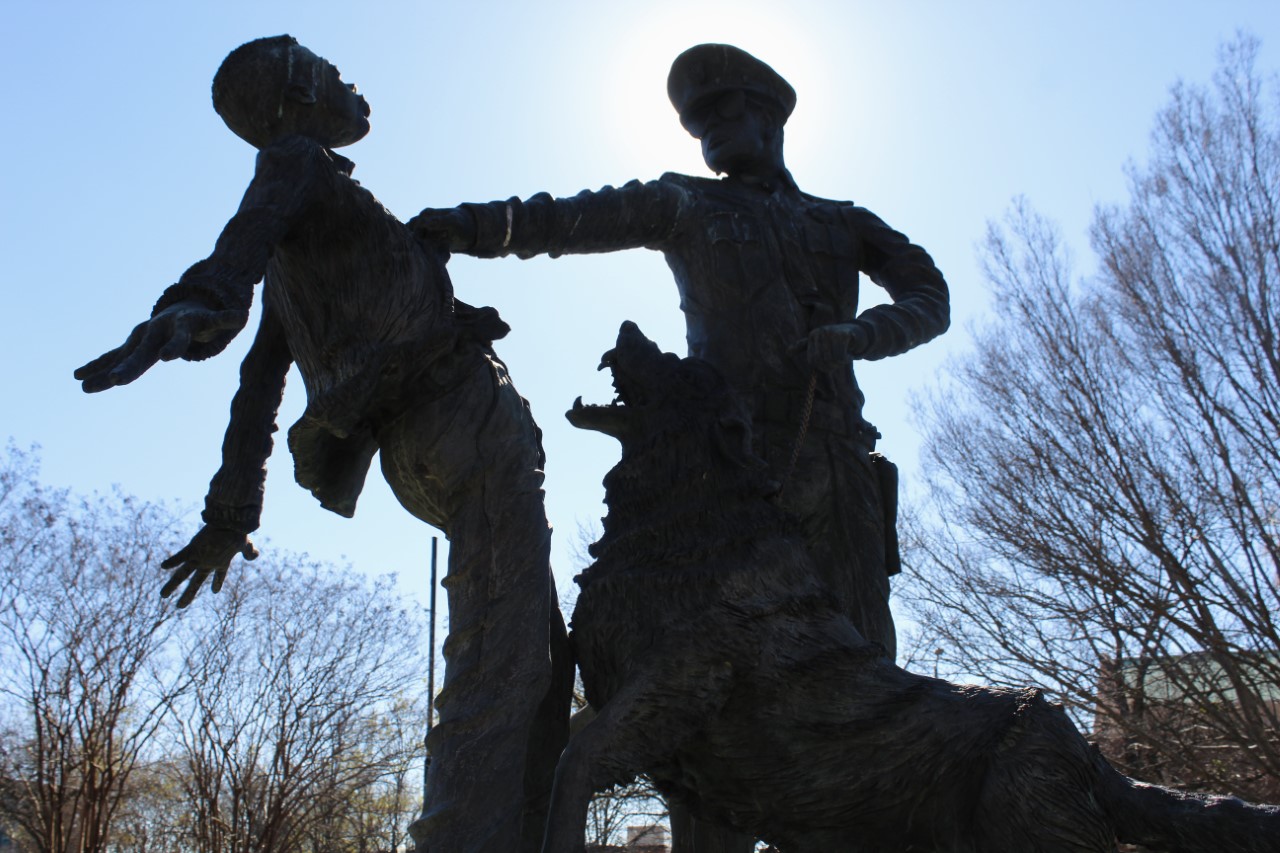 A statue of a child being grabbed by a police officer while a dog attacks the child.