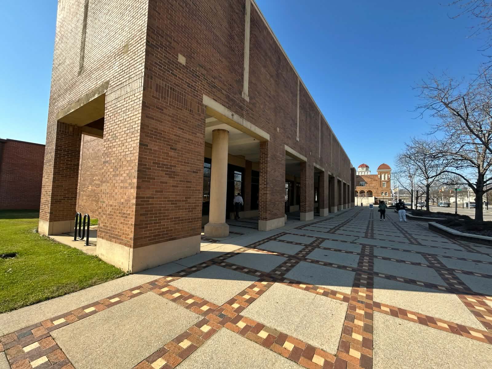 A brick and concrete two story building towers over a patterned sidewalk.