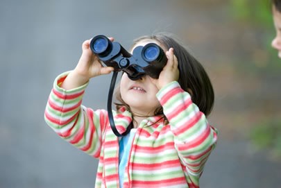 A small child looks through a pair of upside down and backwards binoculars.
