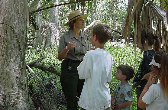 A ranger talks with four children under a tree.
