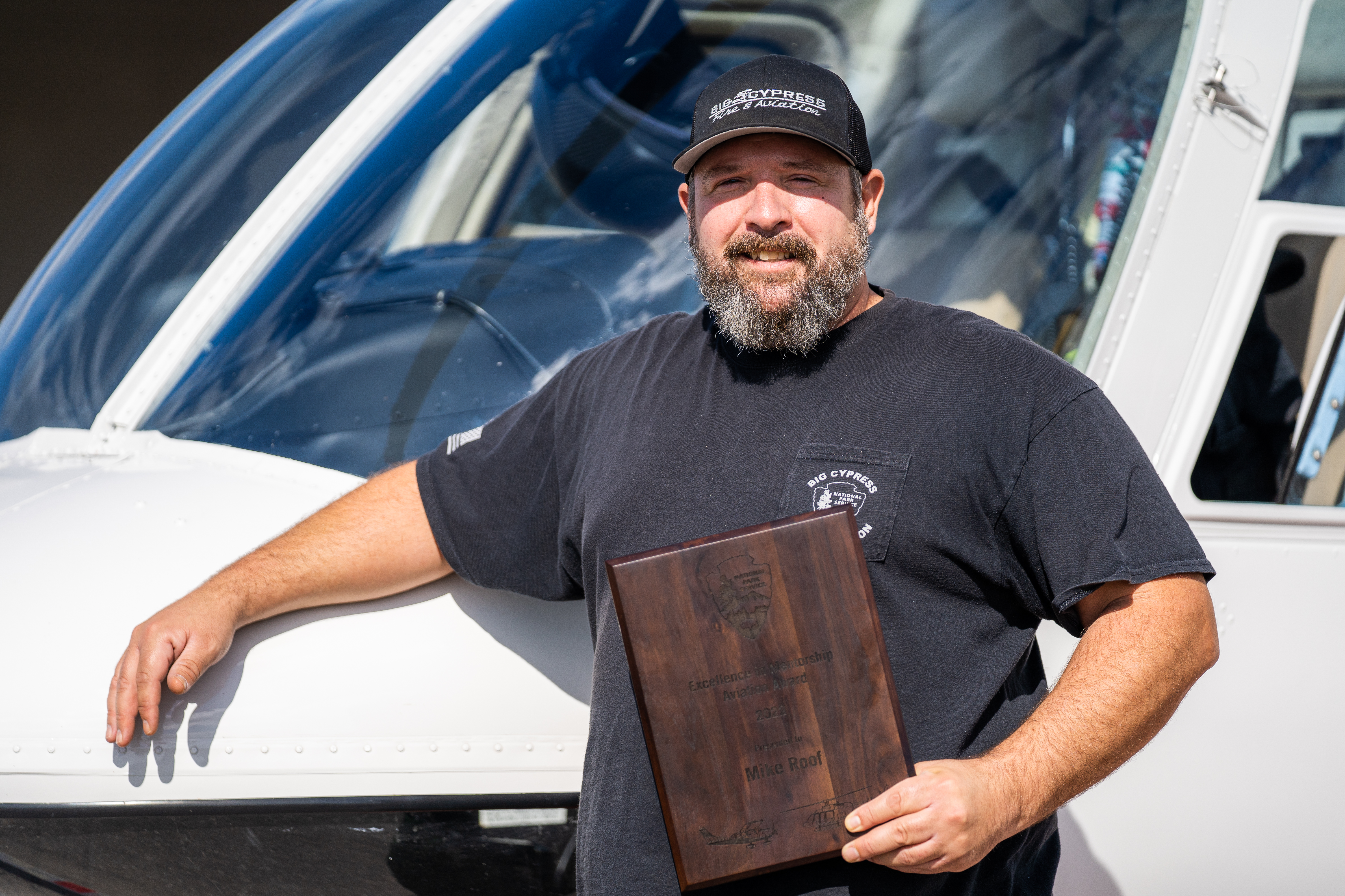 Mike Roof stands in front of helicopter with NPS Excellence Plaque Mike Roof stands in front of helicopter with NPS Excellence Plaque