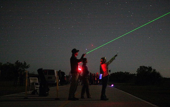 A group of park rangers with a green laser pointing towards the night sky.