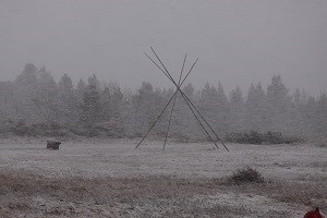 Tepee poles with trees in the distance during snow storm. Tepee poles with trees in the distance during snow storm.
