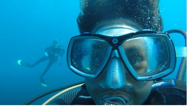 Underwater close up of a scuba diver's face with another diver in the distance