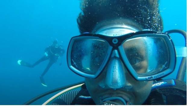 SCUBAnaut Jyvana Murray Underwater close up of a scuba diver's face with another diver in the distance