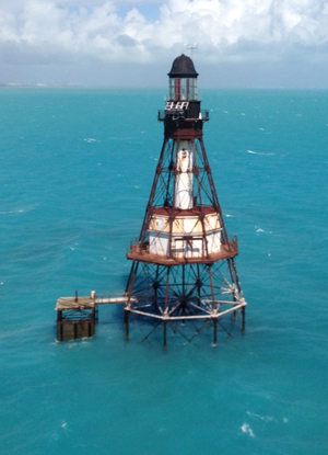 Fowey Rocks Lighthouse stands in turquoise water.