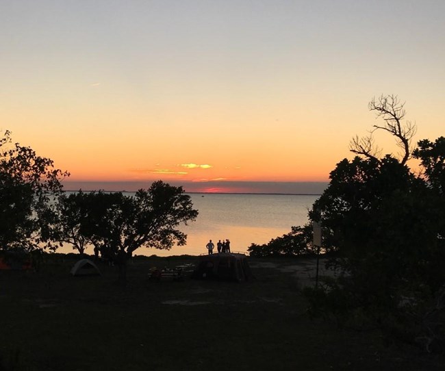 Silhouettes of four people watching an orange and red sunset