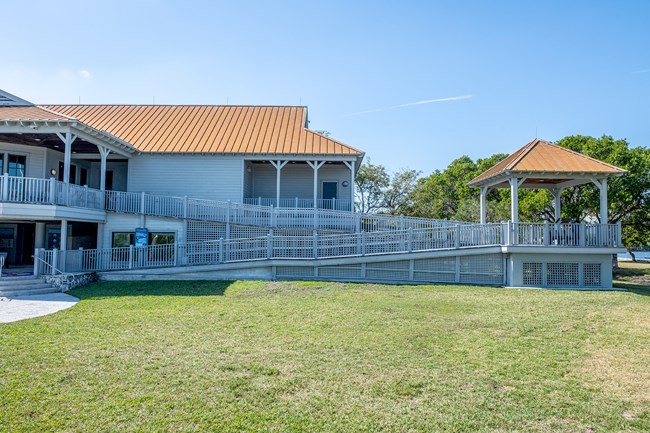 A ramp in two stages leads to the second-floor visitor center. Halfway up the ramp is a roofed flat section with benches and a nice view. Open green lawn spreads across the foreground below.