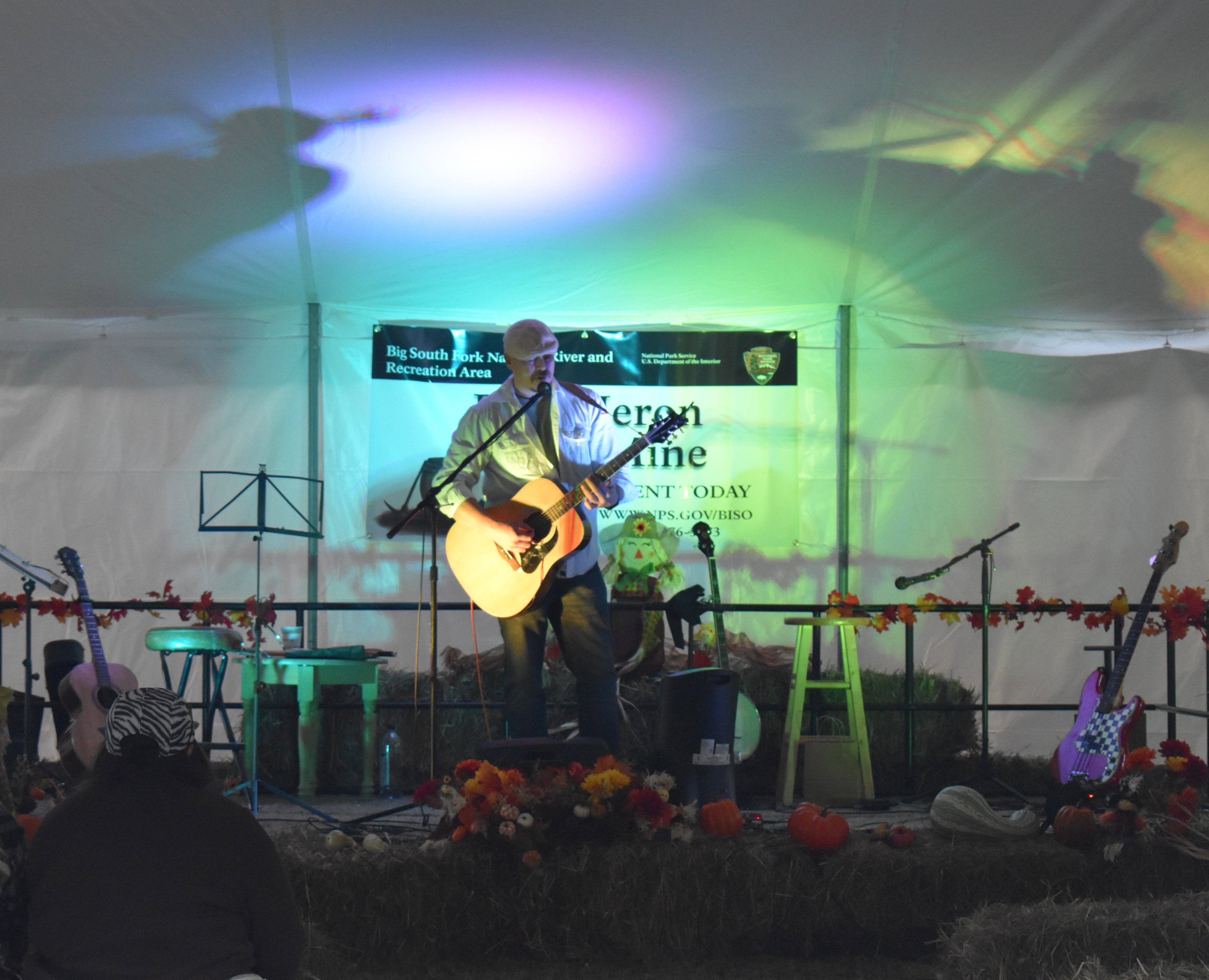 A man sitting on stage with a guitar singing.