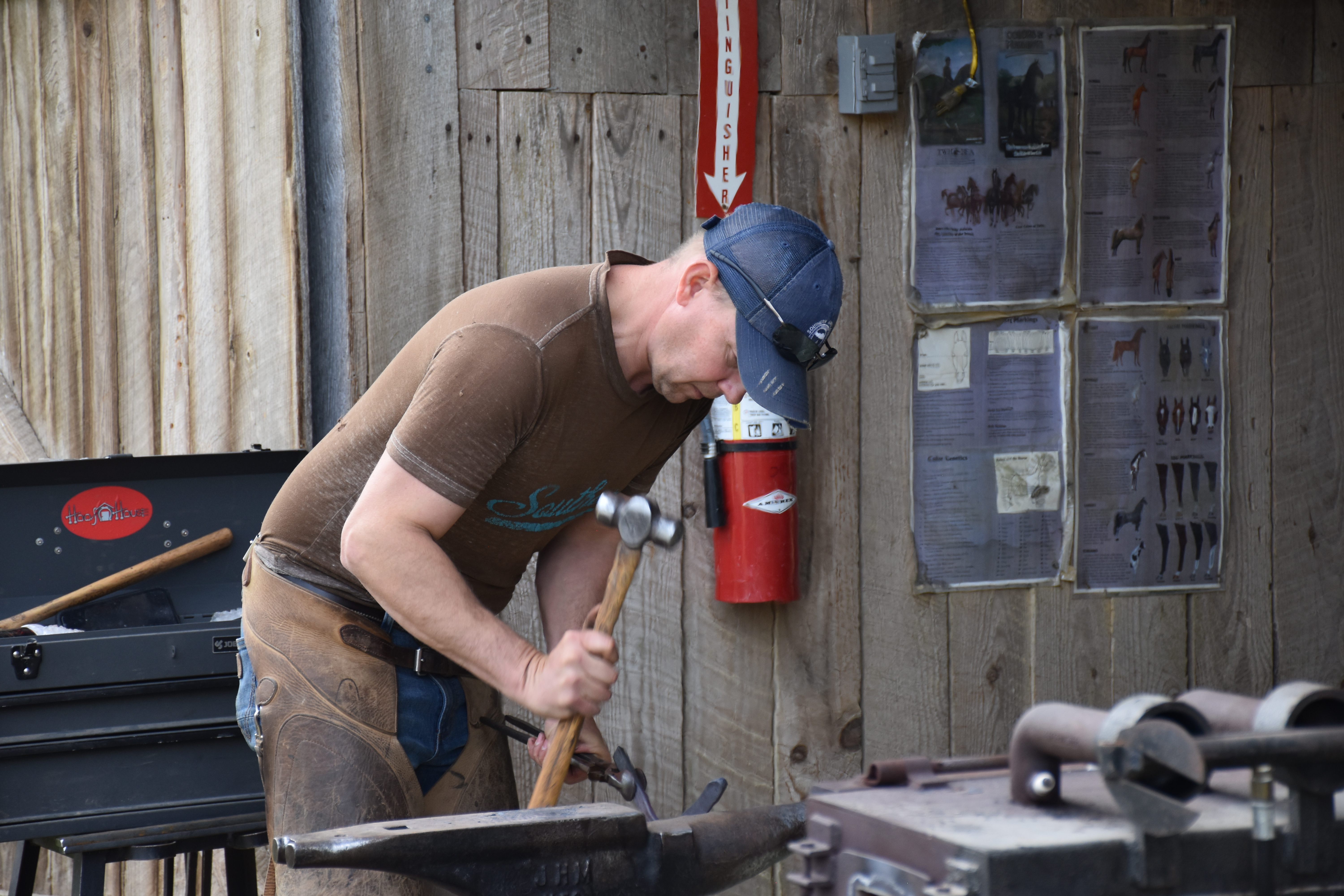 A male working with blacksmithing near a barn.