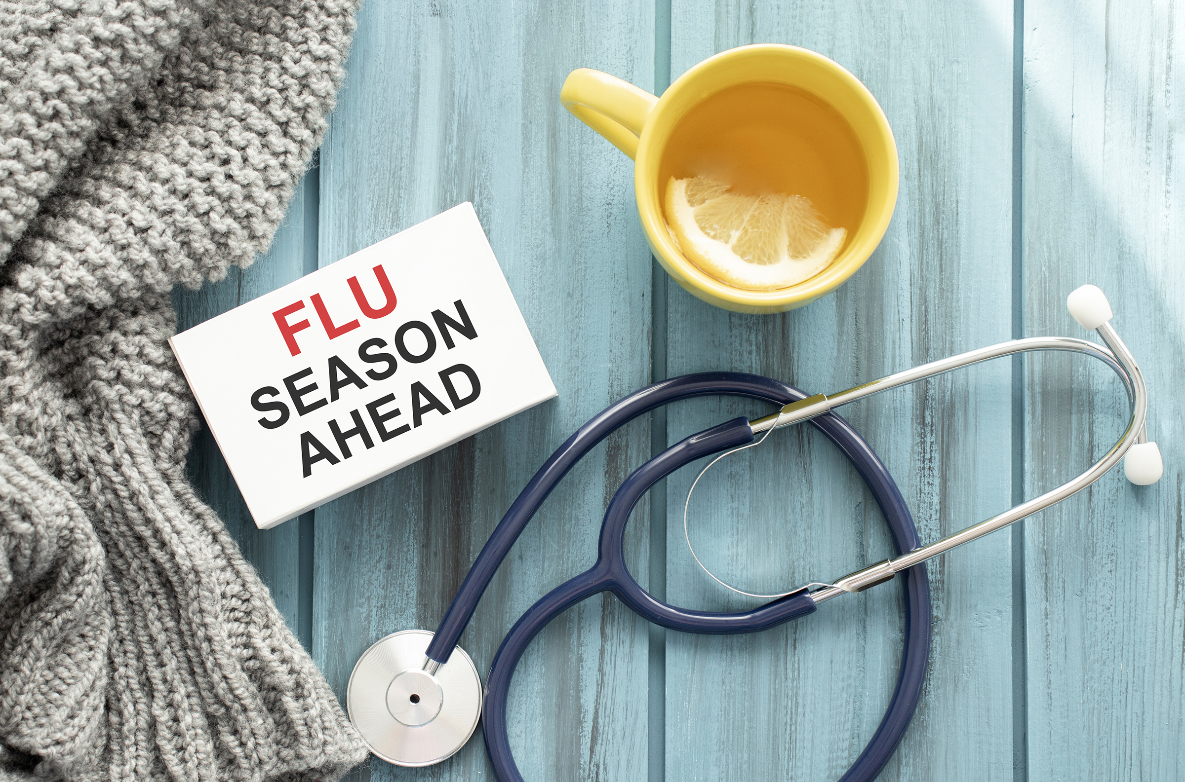 Flu Season A stethoscope, tea, scarf, and a sign reading "Flu Season Ahead" on a blue background.