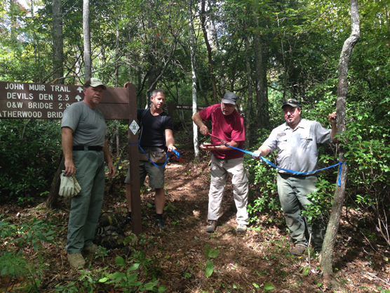 four men standing on trail with ribbon cutting ceremony