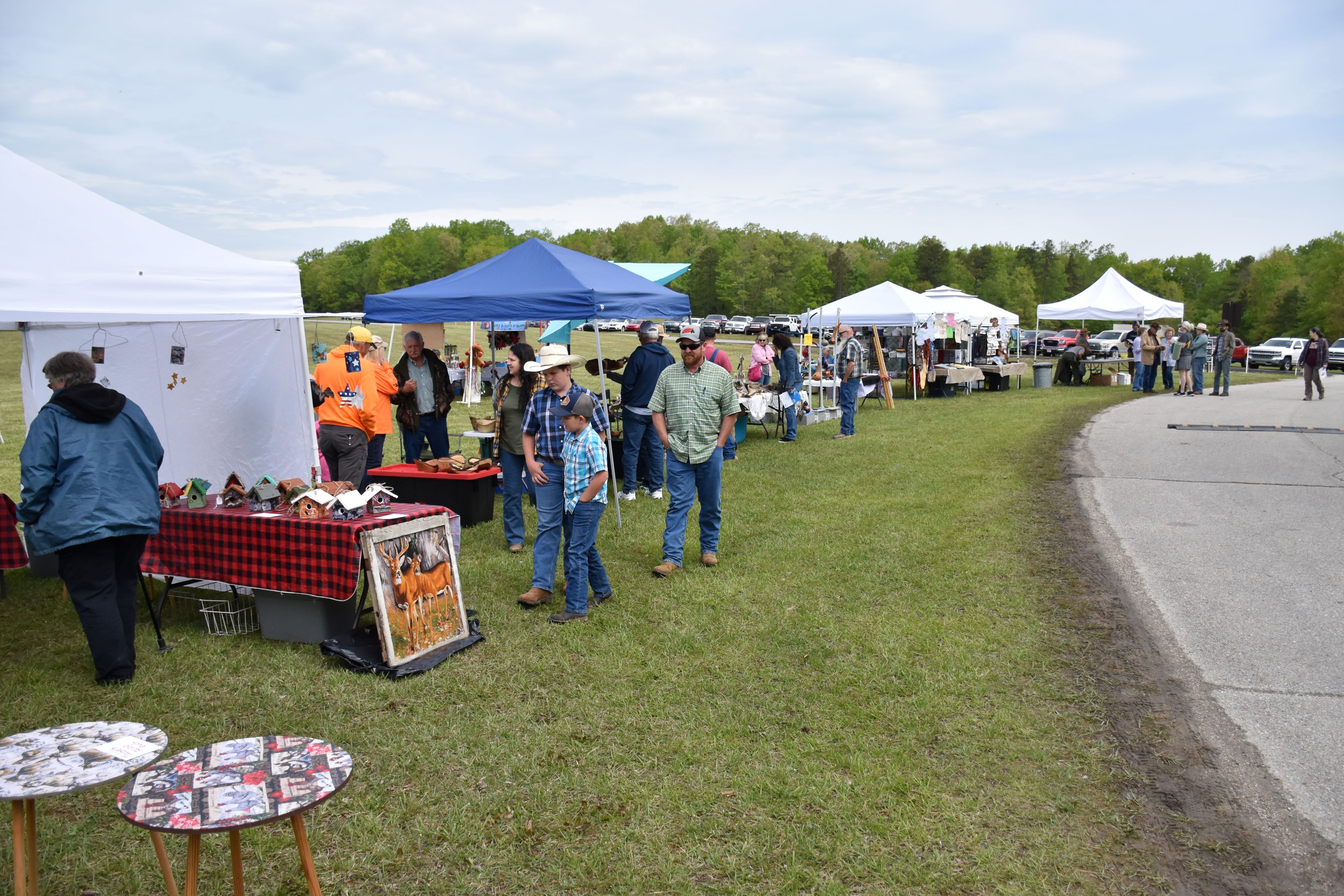 A frow of tents and tables set up for craft vendors and people walking by to look at items.