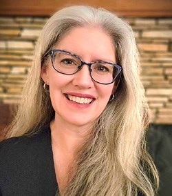 A white female, blonde hair wearing glasses portrait.