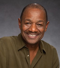 An african american male smiling portrait wearing agreen button down shirt.