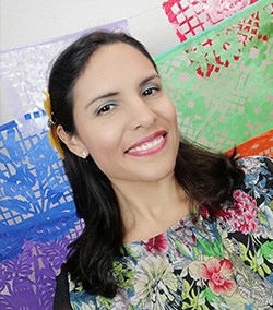 A female smiling at the camera in a floral print and vibrant color background.