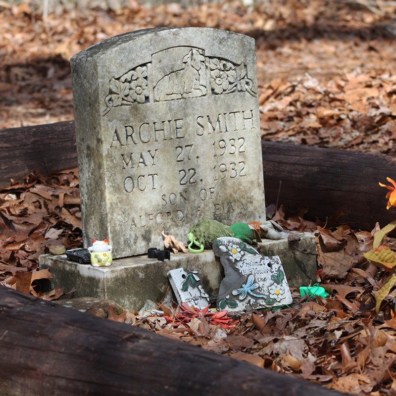 Tombstone with a flower and various small objects around it.