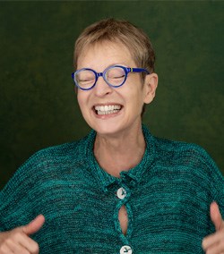 A female with glasses smiling with closed eyes and giving a thumbs up.